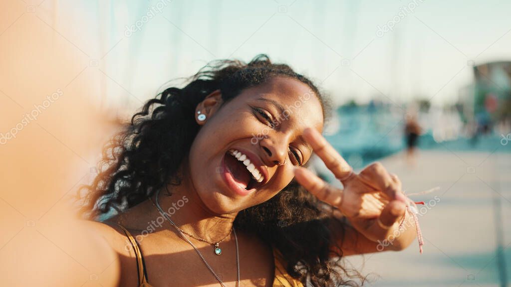 Close-up portrait of smiling girl with long curly hair chatting on the embankment, on yacht background. Frontal closeup of happy young woman using mobile phone