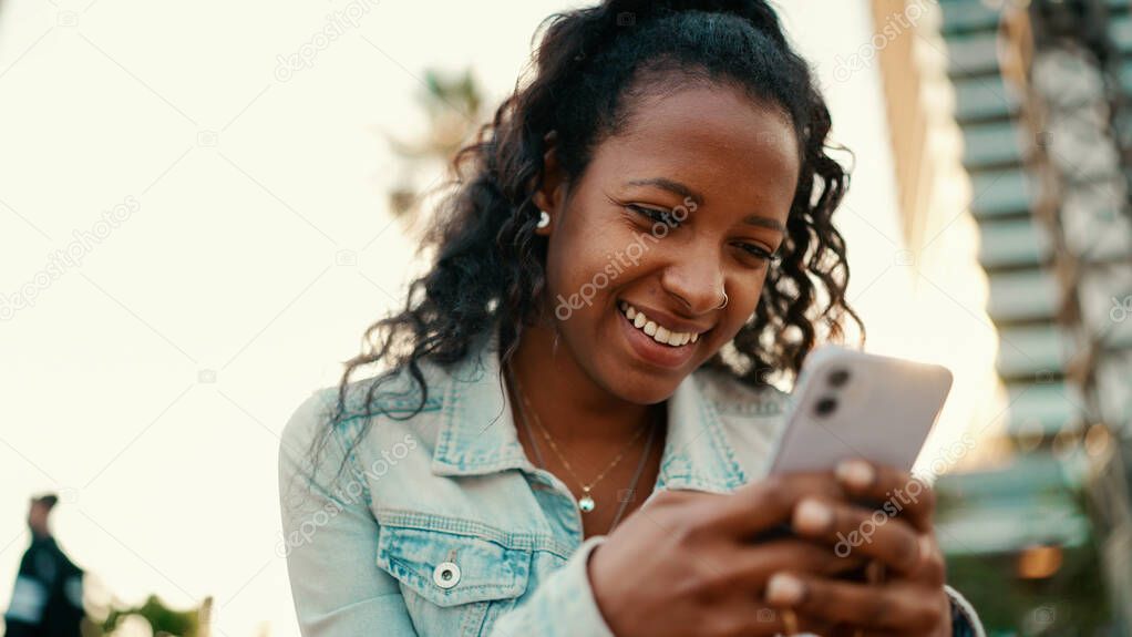 Closeup of young woman with long curly hair using a mobile phone in an urban city background. Close-up of  girl communicating in social networks on a smartphone