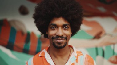 Genç Afro-Amerikan bir adamın yakın plan portresi gözlerini açar kameraya bakar ve kentsel sokak arka planında gülümseyerek durur. Kentsel yaşam. 
