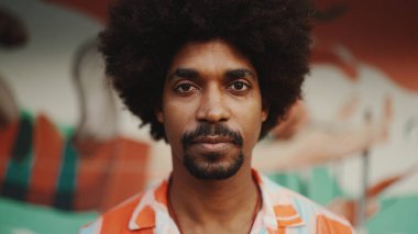 Genç Afro-Amerikan bir adamın yakın plan portresi gözlerini açar kameraya bakar ve kentsel sokak arka planında gülümseyerek durur. Kentsel yaşam. 