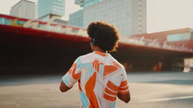 Tişört giyen, kulaklıkla müzik dinleyen ve şehir arka planında dans eden neşeli genç Afrikalı Amerikalı adamın yakın çekimi. Yaşam tarzı kavramı. 