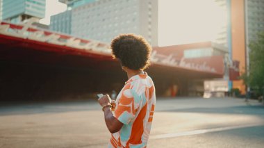 Tişört giyen, kulaklıkla müzik dinleyen ve şehir arka planında dans eden neşeli genç Afrikalı Amerikalı adamın yakın çekimi. Yaşam tarzı kavramı