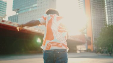 Tişört giyen, kulaklıkla müzik dinleyen ve şehir arka planında dans eden neşeli genç Afrikalı Amerikalı adamın yakın çekimi. Yaşam tarzı kavramı