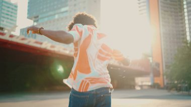 Tişört giyen, kulaklıkla müzik dinleyen ve şehir arka planında dans eden neşeli genç Afrikalı Amerikalı adamın yakın çekimi. Yaşam tarzı kavramı