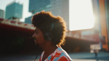 Tişört giyen, kulaklıkla müzik dinleyen ve şehir arka planında dans eden neşeli genç Afrikalı Amerikalı adamın yakın çekimi. Yaşam tarzı kavramı