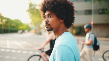 Açık mavi tişörtlü Afro-Amerikan genç adam yaya geçidinde duruyor.. 