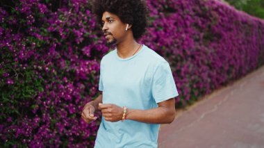 Kapalı kapılar ardında mor çiçeklerle kaplı, kablosuz kulaklıkla müzik dinleyen ve dans eden genç, Afro-Amerikan bir adam. Yaşam tarzı kavramı.