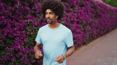 Kapalı kapılar ardında mor çiçeklerle kaplı, kablosuz kulaklıkla müzik dinleyen ve dans eden genç, Afro-Amerikan bir adam. Yaşam tarzı kavramı.