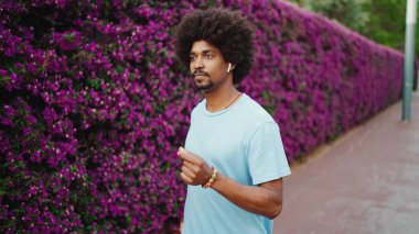 Kapalı kapılar ardında mor çiçeklerle kaplı, kablosuz kulaklıkla müzik dinleyen ve dans eden genç, Afro-Amerikan bir adam. Yaşam tarzı kavramı.