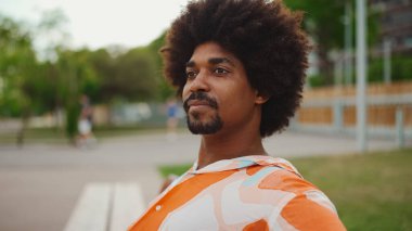 Parktaki bankta rahatça oturan, gömlek giyen Afro-Amerikalı genç adam başka tarafa bakıyor. Yaşam tarzı konsepti. 