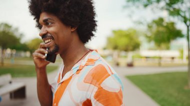 Parktaki yolda yürürken ve akıllı telefondan konuşan Afro-Amerikan genç adamın yakın çekimi. Cep telefonuyla duygusal konuşan bir adam. Yaşam tarzı kavramı. 