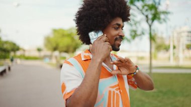 Parktaki yolda yürürken ve akıllı telefondan konuşan Afro-Amerikan genç adamın yakın çekimi. Cep telefonuyla duygusal konuşan bir adam. Yaşam tarzı kavramı. 