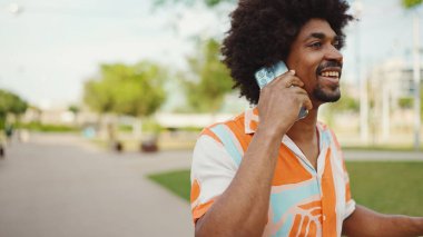 Parktaki yolda yürürken ve akıllı telefondan konuşan Afro-Amerikan genç adamın yakın çekimi. Cep telefonuyla duygusal konuşan bir adam. Yaşam tarzı kavramı. 