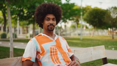 Parktaki bankta rahat bir şekilde kameraya bakarak oturan gülümseyen Afro-Amerikan bir adamın yakın plan portresi. Yaşam tarzı konsepti.