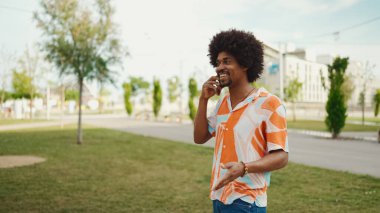 Parktaki yolda yürürken ve akıllı telefondan konuşan Afro-Amerikan genç adamın yakın çekimi. Cep telefonuyla duygusal konuşan bir adam. Yaşam tarzı kavramı. 