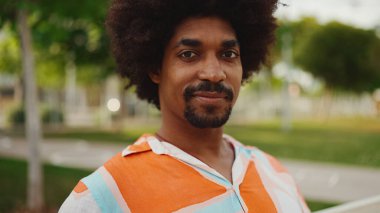 Parktaki bankta rahat bir şekilde kameraya bakarak oturan gülümseyen Afro-Amerikan bir adamın yakın plan portresi. Yaşam tarzı konsepti.