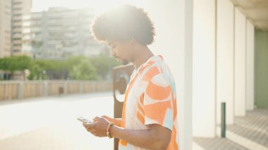 Yakından bakınca, tişört giyen Afro-Amerikalı genç adam sosyal ağlarda şehir arka planında cep telefonuyla yazıyor. Kamera kişiye doğru ilerliyor.. 