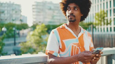 Yakından bakınca, tişört giyen Afro-Amerikalı genç adam sosyal ağlarda şehir arka planında cep telefonuyla yazıyor. Kamera kişiye doğru ilerliyor.. 