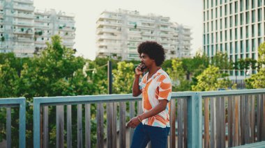 Gömlek giyen ve akıllı telefondan konuşan Afrikalı genç bir adamın yakın çekimi. Yaşam tarzı konsepti. Yavaş çekim geri aydınlatma. 