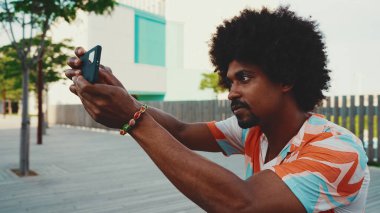 Genç Afro-Amerikan tişört çekimine yakın çekim. Şehir arka planındaki köprüde akıllı telefon tribünlerini kullanın. Yaşam tarzı kavramı