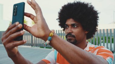 Genç Afro-Amerikan tişört çekimine yakın çekim. Şehir arka planındaki köprüde akıllı telefon tribünlerini kullanın. Yaşam tarzı kavramı