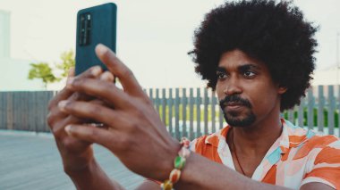 Genç Afro-Amerikan tişört çekimine yakın çekim. Şehir arka planındaki köprüde akıllı telefon tribünlerini kullanın. Yaşam tarzı kavramı