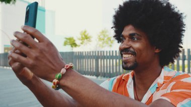 Genç Afro-Amerikan tişört çekimine yakın çekim. Şehir arka planındaki köprüde akıllı telefon tribünlerini kullanın. Yaşam tarzı kavramı