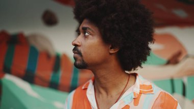 Genç Afro-Amerikan bir adamın yakın plan portresi gözlerini açar kameraya bakar ve kentsel sokak arka planında gülümseyerek durur. Kentsel yaşam. 