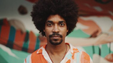 Genç Afro-Amerikan bir adamın yakın plan portresi gözlerini açar kameraya bakar ve kentsel sokak arka planında gülümseyerek durur. Kentsel yaşam. 