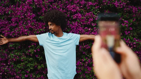 Arkadaki duvarda mor çiçeklerle kaplı fotoğraf standı için poz veren genç Afrikalı Amerikalı adamın yakın çekimi. Yaşam tarzı kavramı