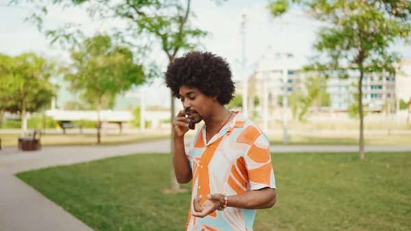 Parktaki yolda yürürken ve akıllı telefondan konuşan Afro-Amerikan genç adamın yakın çekimi. Cep telefonuyla duygusal konuşan bir adam. Yaşam tarzı kavramı. 