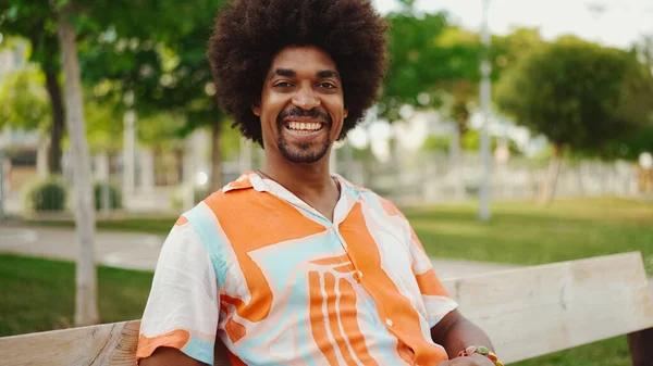 Parktaki bankta rahat bir şekilde kameraya bakarak oturan gülümseyen Afro-Amerikan bir adamın yakın plan portresi. Yaşam tarzı konsepti.