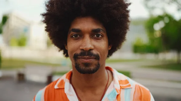 Close-up frontal portrait of young African American man wearing shirt looking at the camera and smiling. Camera moving forwards approaching the person. Lifestyle concept.