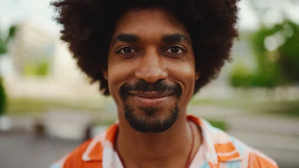 Close-up frontal portrait of young African American man wearing shirt looking at the camera and smiling. Camera moving forwards approaching the person. Lifestyle concept.