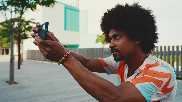 Genç Afro-Amerikan tişört çekimine yakın çekim. Şehir arka planındaki köprüde akıllı telefon tribünlerini kullanın. Yaşam tarzı kavramı