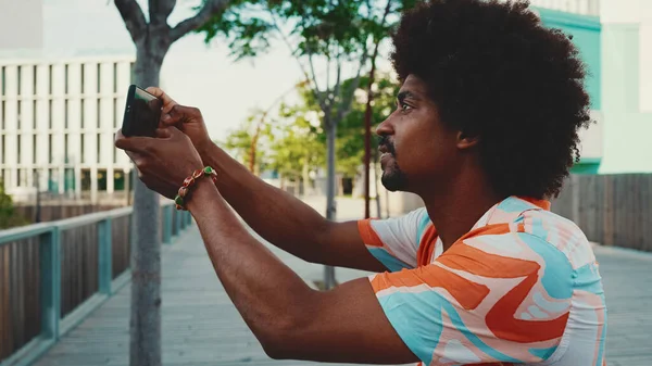 Genç Afro-Amerikan tişört çekimine yakın çekim. Şehir arka planındaki köprüde akıllı telefon tribünlerini kullanın. Yaşam tarzı kavramı