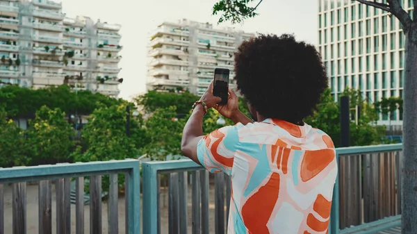 Genç Afro-Amerikan tişört çekimine yakın çekim. Şehir arka planındaki köprüde akıllı telefon tribünlerini kullanın. Yaşam tarzı kavramı