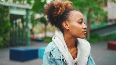 Kot ceketli, güzel, Afro-Amerikalı bir kadın. Etrafına bakıyor..