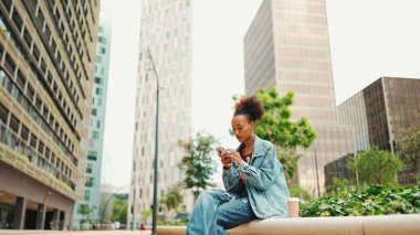 At kuyruklu, kot ceketli Afrikalı bir kız cep telefonuna modern şehir geçmişine karşı sesli mesaj bırakıyor.. 