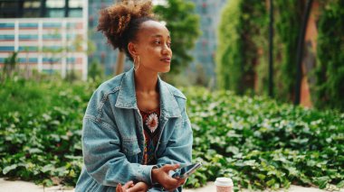 At kuyruklu, kot ceketli Afrikalı bir kız cep telefonuna modern şehir geçmişine karşı sesli mesaj bırakıyor.. 