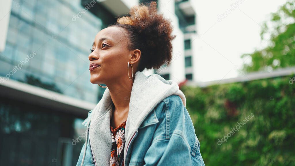 Clouse-up of nice young African American woman with ponytail in denim jacket looking around.
