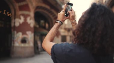 Uzun kıvırcık saçlı ve sakallı çekici İtalyan adam eski bir binanın fotoğrafını çekiyor. Kulağında küpe ve bir sürü zincire bağlı şık bir adam manzara çekiyor. Arka plan