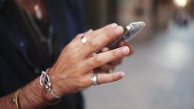 Erkek eli bilezik ve halkalarla cep telefonunda gezinen bilgilerin yakın plan görüntüsü