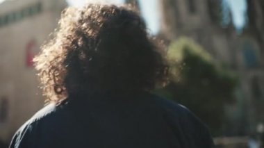 Uzun kıvırcık saçlı ve sakallı genç İtalyan adam aromatik kahvenin tadını çıkarıyor. Tarz sahibi bir adam eski şehrin arka planında kahve içer. Kamera hareket ediyor