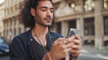 Uzun kıvırcık saçlı ve sakallı çekici İtalyan çocuk cep telefonu kullanıyor. Akıllı telefondan mesaj yazan şık bir adam.