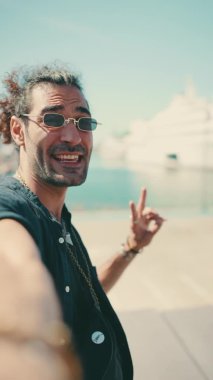 Uzun kıvırcık saçlı ve sakallı genç bir İtalyan cep telefonundan selfie çekiyor. Güneş gözlüklü şık adam akıllı telefonunun kamerasına gülümsüyor.