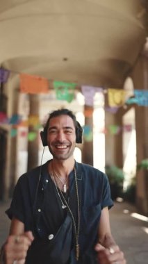 Kulaklıklı at kuyruklu ve sakallı genç İtalyan adam şehir manzarası arka planına gider. Tarz sahibi adam kulaklıkla müzik dinliyor ve dans ediyor.