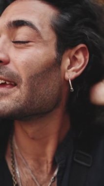 Clouse-up, uzun kıvırcık saçlı ve sakallı çekici İtalyan adam cep telefonu kullanıyor. Kulağında küpe olan şık bir adam ve akıllı telefondan konuşan bir sürü zincir.