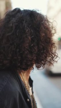 Uzun kıvırcık saçlı ve sakallı adam yaya geçidinin önündeki kaldırımda dururken güneş gözlüğü takıyor. Yaya geçidinin önünde dikilen şık bir adam etrafa bakıyor.