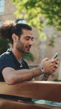 At kuyruklu ve sakallı çekici İtalyan adam eski binaların arkasındaki bankta otururken cep telefonu kullanıyor. Tarz sahibi adam bilgilere bakar, akıllı telefondan fotoğraf çeker.